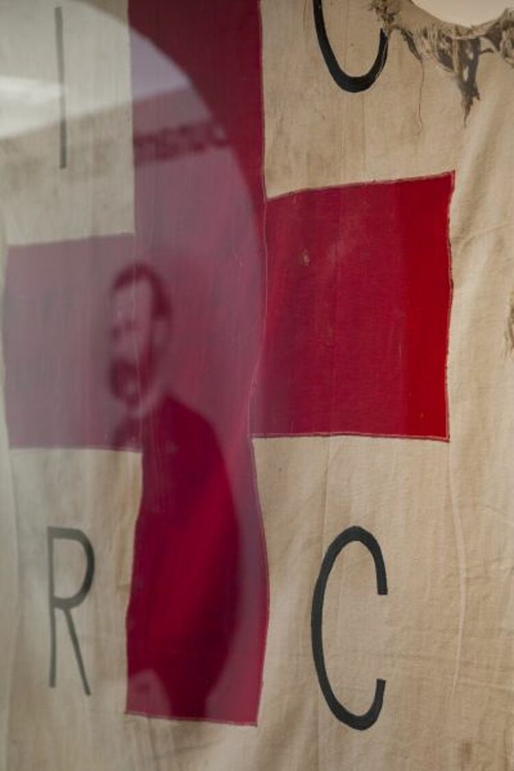 Im Henry-Dunant-Museum im schweizerischen Heiden spiegelt sich sein Porträt in einer Vitrine mit einer zerschlissenen Rotkreuzfahne, die während des Bürgerkriegs in Angola benutzt wurde (Jörg F. Müller / DRK) Im Henry-Dunant-Museum im schweizerischen Heiden spiegelt sich sein Porträt in einer Vitrine mit einer zerschlissenen Rotkreuzfahne, die während des Bürgerkriegs in Angola benutzt wurde (Jörg F. Müller / DRK)